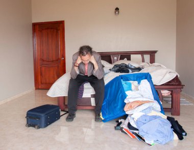 At kuyruklu bir adam odasında oturmuş kıyafetlerinin ve bavulunun nasıl dağınık olduğunu ve yere fırlatıldığını izliyor.