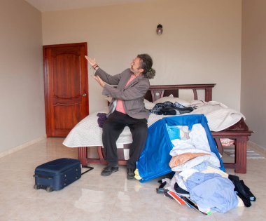 At kuyruklu bir adam odasında oturmuş kıyafetlerinin ve bavulunun nasıl dağınık olduğunu ve yere fırlatıldığını izliyor.