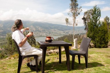 man dressed in white sitting on a chair on top of a mountain drinking a hot coffee in a cup watching the sunrise clipart