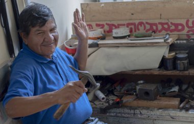 shoemaker sitting at his work table while greeting the camera very kindly