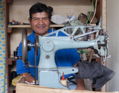 smiling shoemaker looking at camera in his shoe store while fixing shoes
