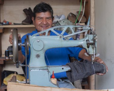smiling shoemaker looking at camera in his shoe store while fixing a woman's boot