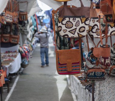 bag with Andean design hanging in a stall in a market in Ecuador with an indigenous man in the background