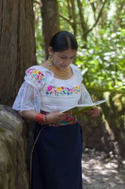 Yerli kadın yemyeşil bir arazide kitap okuyor.