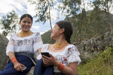2 indigenous people in nature sending a text message with a mobile device very happy. High quality photo