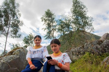 Two female friends using internet on mobile on the top of the mountain with a modern smartphone. High quality photo