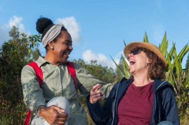 Farklı babaların kız kardeşleri yürüyüş yaptıktan sonra bir dağda dinlenirken kahkahalarla gülüyorlar. Yüksek kalite fotoğraf