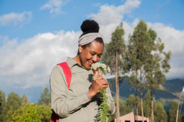Dağlardaki afro kadın sevimli bir gülümsemeyle beyaz çiçeklerin hoş kokusunu alıyor. Yüksek kalite fotoğraf