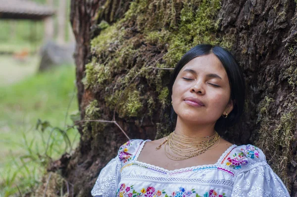 Indigenous woman with her traditional dress lying on a tree full of moss in the jungle of Ecuador. woman feeling mother nature in a moment of mental well-being and peace. Earth day. High quality photo