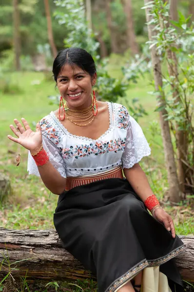 sweet indigenous woman from ecuador sitting on a fallen tree in a forest smiling and waving to the camera. High quality photo