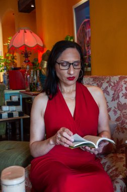 50 'li yaşlarda çok zarif bir kadının portresi klasik ve huzurlu bir ortamda kırmızı ve beyaz bir kanepede kitap okuyor. Kitap günü. Yüksek kalite fotoğraf