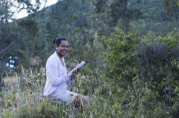 copyspace of an old afro woman sitting on a stone in the middle of the nature with a book in her hand and smiling to the camera, book day. High quality photo