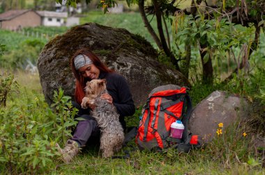 Sırt çantasının yanında köpeğiyle oynayan, bir kayanın üzerinde dinlenen bir aşık kız. Yüksek kalite fotoğraf