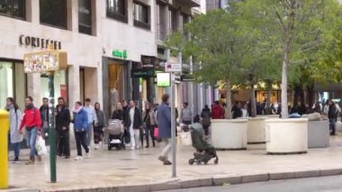 Kentsel bir çevrede, dükkan ve ağaçların önünden geçen yayalar ve müşteriler hakkında çok sayıda görüş var.