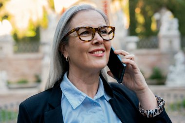 Kendinden emin yaşlı bir kadın akıllı telefonunu ustalıkla kullanır, profesyonellik ve çekicilik yayar.