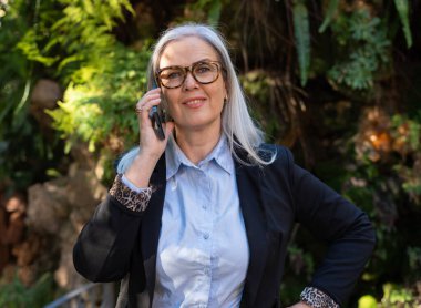 Şık bir kadın, güzel doğal ortamının tadını çıkarırken kendine güvenerek bir telefon görüşmesi yapar.