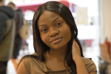 Kendine güvenen ve şık, genç siyah bir kadın uzun, siyah saçlarına nazikçe dokunuyor, dingin ifadesi yumuşak, bulanık bir arka plana karşı cezbedici, muhtemelen umumi bir alanda.