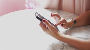 Bir kişi şık bir kafede otururken akıllı telefonla iletişim kuruyor..