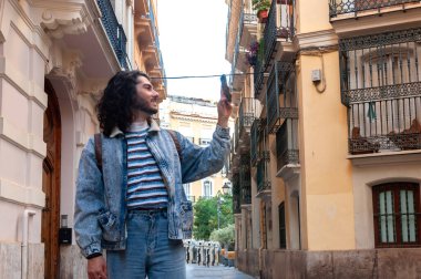 Genç turist büyüleyici bir Avrupa şehrini keşfediyor, akıllı telefonuyla tarihi binalar ve balkonlarla dolu dar bir sokakta gezinirken anları yakalıyor.