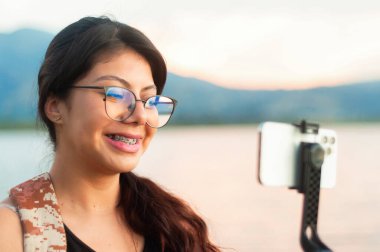 Neşeli genç bir kadın gölün kenarında gün batımının çarpıcı bir selfie 'sini yakalıyor. Neşesini yansıtıyor.