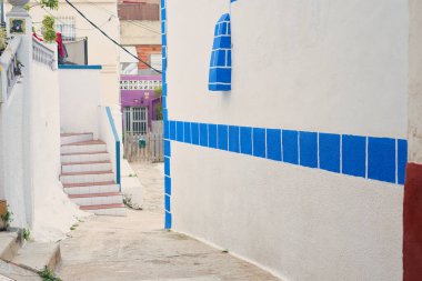 Beyaz duvarları ve çevrenin güzelliğini arttıran parlak mavi karoları olan büyüleyici bir sokak.