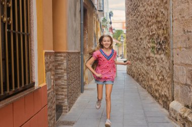 Genç bir kız neşeyle güzel renkli bir sokakta koşar, çocukluk macerasının saf özünü yakalar.