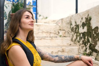 Canlı ve sanatsal bir mahallede genç bir kadın merdivenlerde oturuyor, hayatını ve hayallerini yansıtıyor.