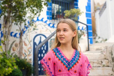 Uzun saçlı, canlı, geleneksel bir elbise giyen genç bir kız açık havada poz veriyor..