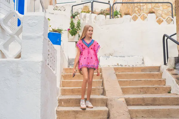 Neşeli genç bir kız neşeli bir şekilde güneşli basamaklarda duruyor, çarpıcı bir ortamda canlı bir kıyafet giyiyor.