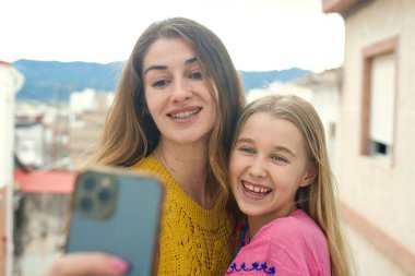 Neşeli bir anne ve kızı mutlu bir şekilde selfie çekerler, güzel bir şehir zeminine karşı parlak bir gülümsemeyle.