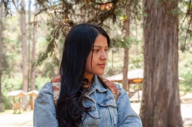 Genç bir kadın düşünceli bir şekilde sakin bir ormana bakıyor. Huzur ve sükunetle dolu güzel bir anı yakalıyor.