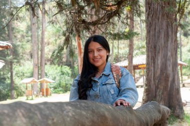 Neşeli ve gülümseyen genç bir kadın, huzurlu ve huzurlu orman manzarasının ortasında neşeli bir şekilde poz verir.