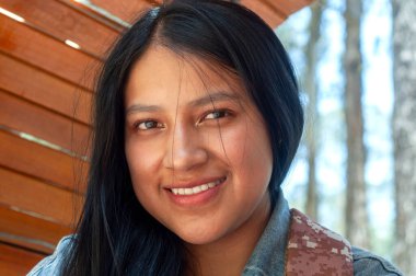 Güzel, doğal bir ortamda, uzun dalgalı saçları olan genç bir kadın sıcak bir şekilde gülümserken neşe ve güven saçar.