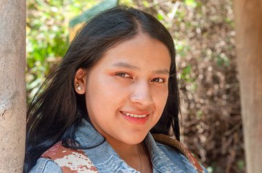 Neşeli genç bir kadın neşeli bir şekilde dışarıda poz veriyor, doğal güzelliğini ve canlı çevresini gösteriyor.