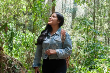 Bir kadın, canlı yeşil bir ormanda yürürken doğanın çarpıcı güzelliğine hayret eder.