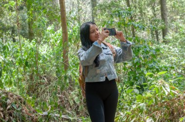 Genç bir kadın coşkuyla doğanın nefes kesici güzelliğini yakalar ve canlı yeşil orman patikalarını keşfeder.