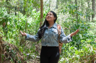 Bir kadın canlı bir ormanda neşeli bir şekilde duruyor, doğanın güzelliğini kucaklıyor kolları açık ve parlak bir gülümsemeyle