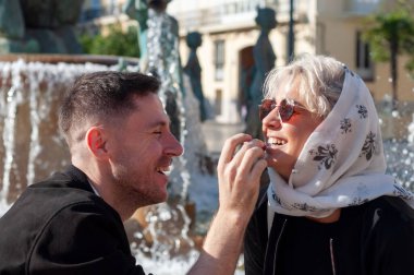 Bir çeşmenin yanındaki neşeli bir etkileşim yakın arkadaşlar arasındaki neşe dolu bir tımar ve şefkat anını resmediyor.