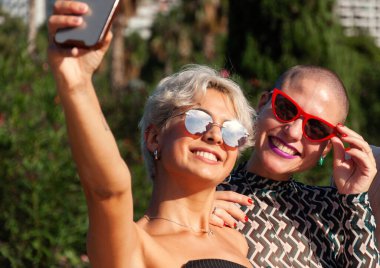İki modaya uygun arkadaş güneşli ve güzel bir günün tadını çıkarıyorlar. Neşeli bir selfie çekiyorlar.