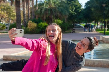 İki yakın arkadaş neşeli ve neşeli bir selfie çeker güzel güneşli bir günde canlı, renkli bir parkta.