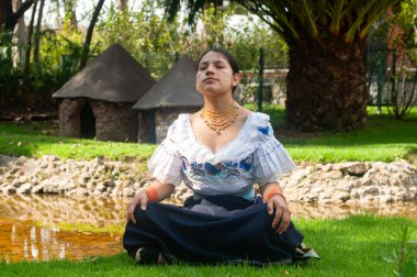 Güzel geleneksel kıyafetler giymiş bir kadın, doğayla çevrili sakin bir gölette huzur içinde meditasyon yapıyor.