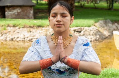 Geleneksel giyinmiş bir kadın, huzur dolu bir suyun yanında, iç huzuru yansıtan huzurlu bir dua pozu verir.