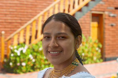 Genç bir kadın ışıl ışıl gülümser, gösterişli geleneksel giysiler ve süslü bir arkaplanda karmaşık mücevherler sergiler..