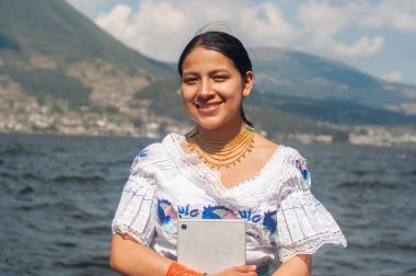 Geleneksel kıyafetlerini giymiş neşeli genç bir kadın, resimli bir dağ gölünün yanında gururla durur.