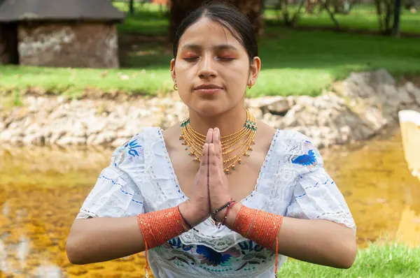 Geleneksel giyinmiş bir kadın, huzur dolu bir suyun yanında, iç huzuru yansıtan huzurlu bir dua pozu verir.