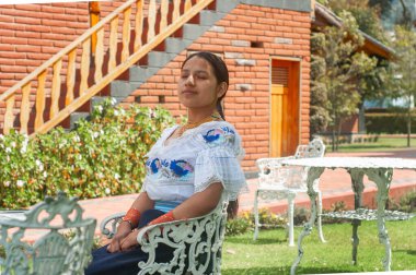 Huzurlu bir sahnede zarif geleneksel giysiler içinde güzel bir bahçede oturan bir kadın görülüyor.