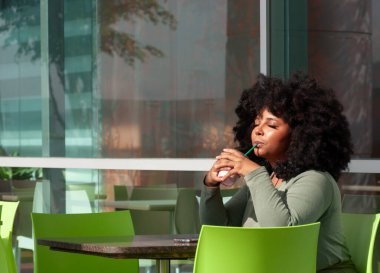 Bir kadın yeşil aksanlı şık bir kafede içmekten zevk alır.