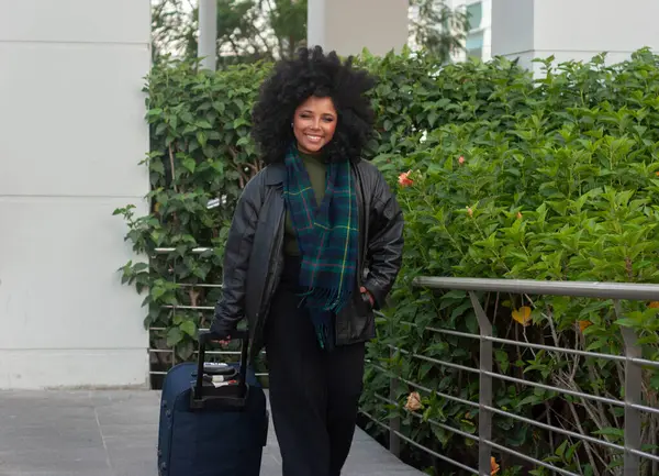 Modaya uygun bir kadın şık bavuluyla, canlı ve gür yeşilliklerle çevrili duruyor.