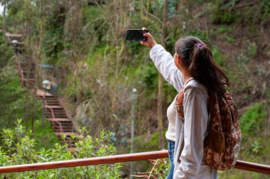 Genç bir gezgin, arka planda büyüleyici adımları olan canlı, yeşil bir ortamda neşeli bir selfie çeker.