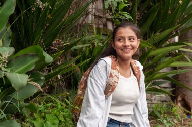 Genç bir kadın, canlı bir yeşillik örtüsüyle çevrili iken sıcak bir şekilde gülümsüyor, neşe ve macerayı somutlaştırıyor.